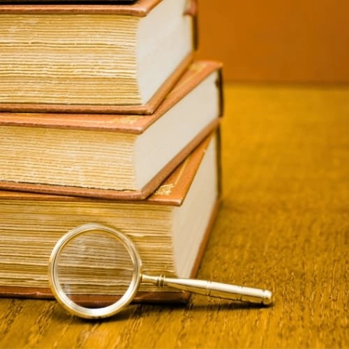 Pile de vieux livre avec une loupe qui représente le service de recherche de mots-clés de Ly Rédaction